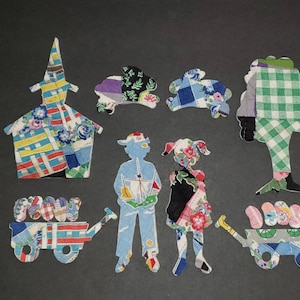 May include: A collection of fabric cutouts in various shapes, including a church, rabbits, children, a tree, and wagons. The cutouts are made from patterned fabrics in blue, yellow, green, and floral designs, set against a dark background.