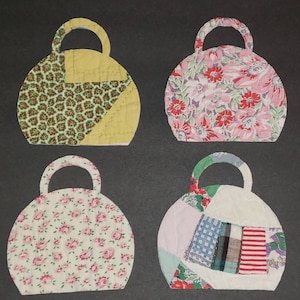 May include: Four quilted fabric handbags in different patterns. The handbags are shaped like a traditional purse with a handle at the top. The patterns include floral, geometric, and patchwork designs.