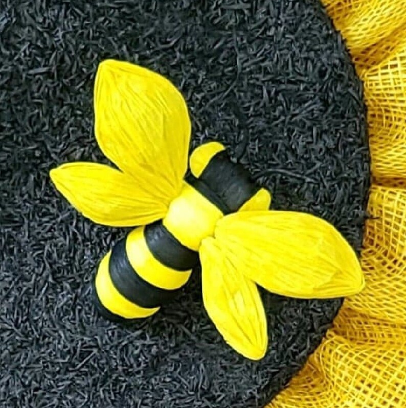 Puede incluir: Una abeja amarilla y negra con alas de papel amarillo. La abeja est&aacute; sentada sobre un fondo negro.