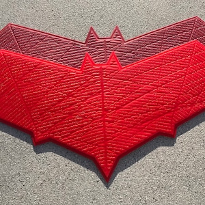 Könnte beinhalten: Zwei rote Fledermaus-Wanddekorationen mit einer strukturierten Oberfläche. Die obere Fledermaus ist in einem dunkleren Rotton.