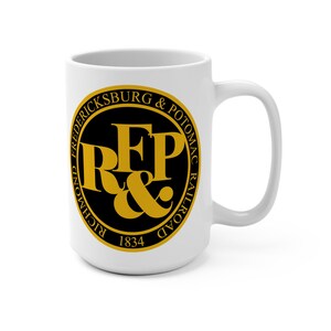 May include: White ceramic mug featuring the Richmond, Fredericksburg & Potomac Railroad logo in black and gold. The logo includes the letters "RFP" and the year 1834, set within a circular design. The mug has a curved handle.