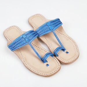 Könnte beinhalten: Ein Paar blaue Ledersandalen mit aufwendigen Nähten und einer Zehenschlaufe. Die Sandalen haben eine beige Ledersohle.