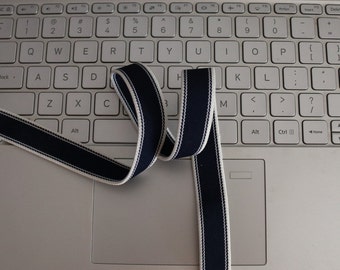 May include: A blue and white striped ribbon is lying on a white laptop keyboard. The ribbon is folded in a loop shape.