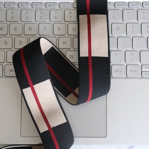 May include: Black and white elastic band with red stripes. The band is folded and placed on a white laptop keyboard.