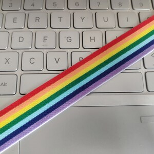 May include: Rainbow striped elastic band on a white laptop keyboard. The elastic band has red, orange, yellow, green, blue, indigo, and violet stripes.