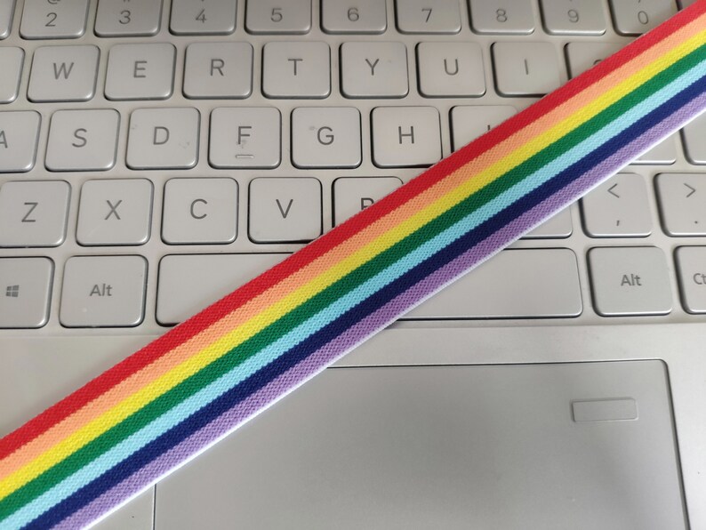 May include: Rainbow striped elastic band on a white laptop keyboard. The elastic band has red, orange, yellow, green, blue, indigo, and violet stripes.