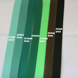 May include: A close-up of ten different shades of green elastic ribbon. The colours are labelled from left to right: 31 Light Green, 30 Moss Green, 29 Jungle Green, 28 Green, 27 Lemon Green, 26 Army Green, 25 Dark Green.