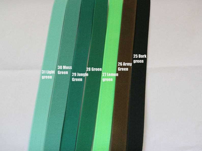May include: A close-up of ten different shades of green elastic ribbon. The colours are labelled from left to right: 31 Light Green, 30 Moss Green, 29 Jungle Green, 28 Green, 27 Lemon Green, 26 Army Green, 25 Dark Green.