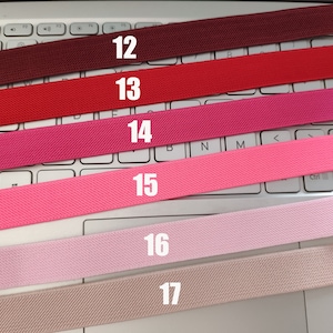 May include: Six different colors of elastic bands, numbered 12 through 17, are laid out on a white keyboard. The colors are burgundy, red, pink, light pink, pale pink, and beige.