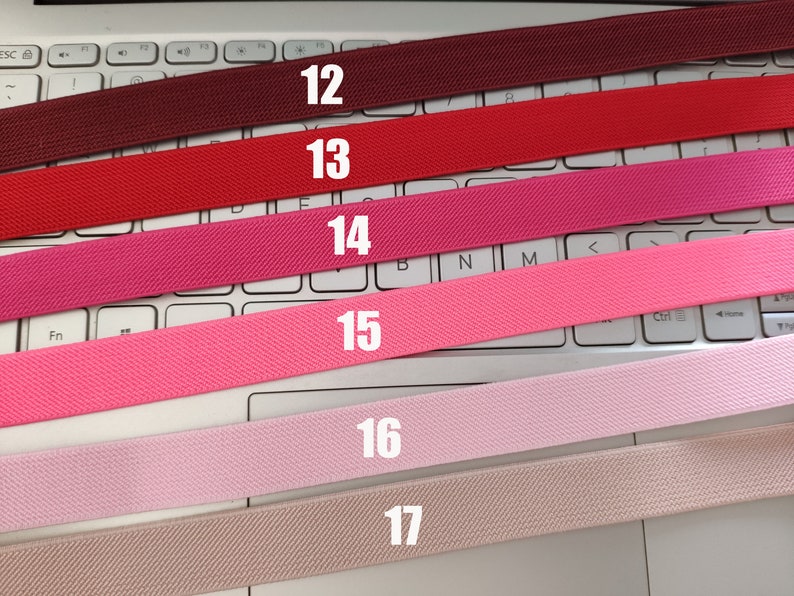 May include: Six different colors of elastic bands, numbered 12 through 17, are laid out on a white keyboard. The colors are burgundy, red, pink, light pink, pale pink, and beige.