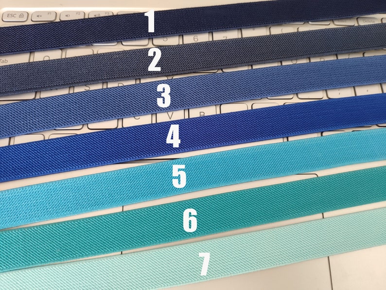 May include: Seven different colors of elastic bands, ranging from dark blue to light blue. The elastic bands are numbered 1 through 7.
