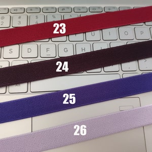 May include: Four different colors of elastic bands, red, brown, purple, and light purple, are laid out on a white keyboard. The bands are numbered 23, 24, 25, and 26.