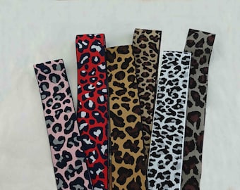 May include: An assortment of leopard print ribbons in various colors, including pink, red, brown, and black. The ribbons are arranged side by side, showcasing the different patterns and color combinations. The ribbons are likely used for crafting or decorative purposes.