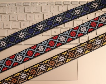 May include: Three black elastic bands with different colored embroidered patterns. The patterns are geometric and feature white, blue, red, and yellow thread.