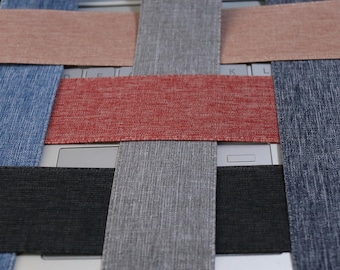 May include: A close-up of woven fabric samples in various colors, including red, gray, black, and blue. The fabric is woven in a criss-cross pattern.