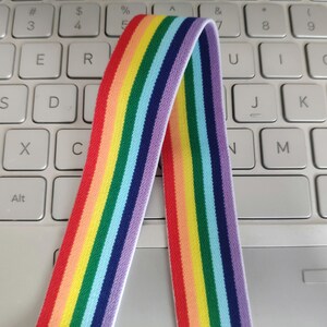 May include: Rainbow striped elastic band with a white background. The band is folded in half and is lying on a white keyboard.
