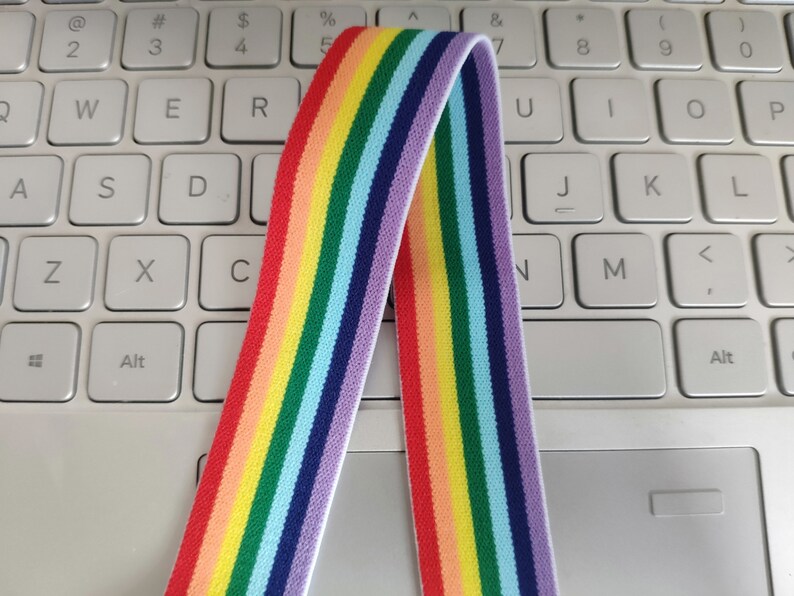 May include: Rainbow striped elastic band with a white background. The band is folded in half and is lying on a white keyboard.