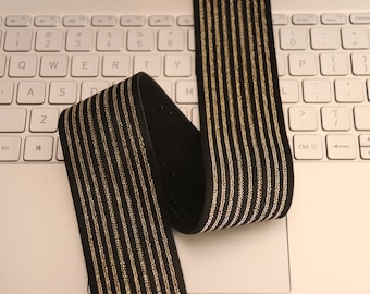 May include: Black elastic with gold stripes. The elastic is folded and lying on a white laptop keyboard.