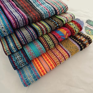 以下が含まれることがあります： 幾何学模様のカラフルな模様のファブリックトリムが積み重ねられています。トリムは織り生地で作られており、青、赤、黄、緑など、さまざまな色があります。