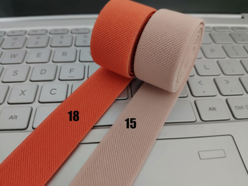 May include: Two rolls of elastic fabric, one orange and one beige, with the numbers "18" and "15" printed on them.