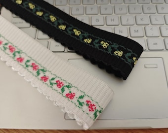 Puede incluir: Dos piezas de ribete elástico con motivos florales. Una es negra con flores amarillas y verdes, la otra es blanca con flores rojas y verdes.