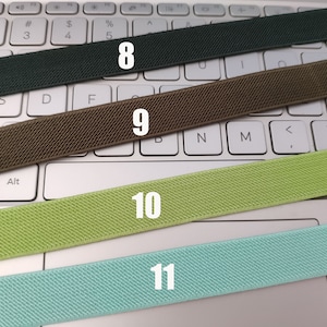 May include: Four different colors of elastic bands laid out on a white keyboard. The bands are labeled 8, 9, 10, and 11.