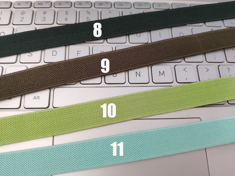 May include: Four different colors of elastic bands laid out on a white keyboard. The bands are labeled 8, 9, 10, and 11.