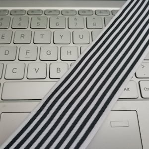 May include: Black and white striped elastic band. The band is lying on a white laptop keyboard.