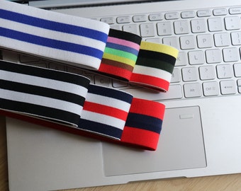 May include: Assortment of colorful elastic bands with striped patterns in blue, black, red, and multi-colored designs. The bands are displayed on a laptop keyboard, showcasing their various color combinations and textures. These bands are likely used for crafting or apparel.