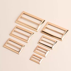 May include: Set of six gold-toned metal slider buckles in various sizes. The buckles are rectangular with two horizontal bars.