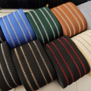 May include: Assortment of striped elastic webbing in various colors, including black, white, blue, green, brown, and red. The webbing has a herringbone pattern and is approximately 1 inch wide.