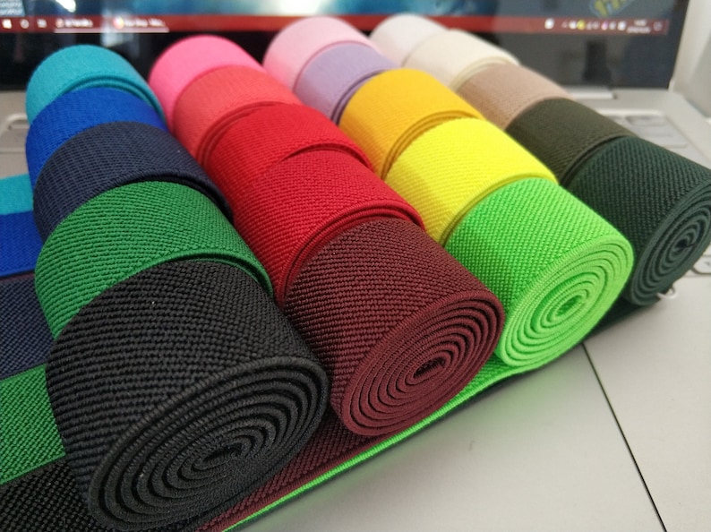 May include: A selection of elastic bands in various colours, including black, green, red, maroon, yellow, and green. The elastic bands are rolled up and stacked on top of each other.