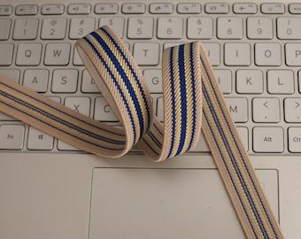 May include: Beige elastic band with blue and yellow stripes. The band is folded and placed on a white laptop keyboard.