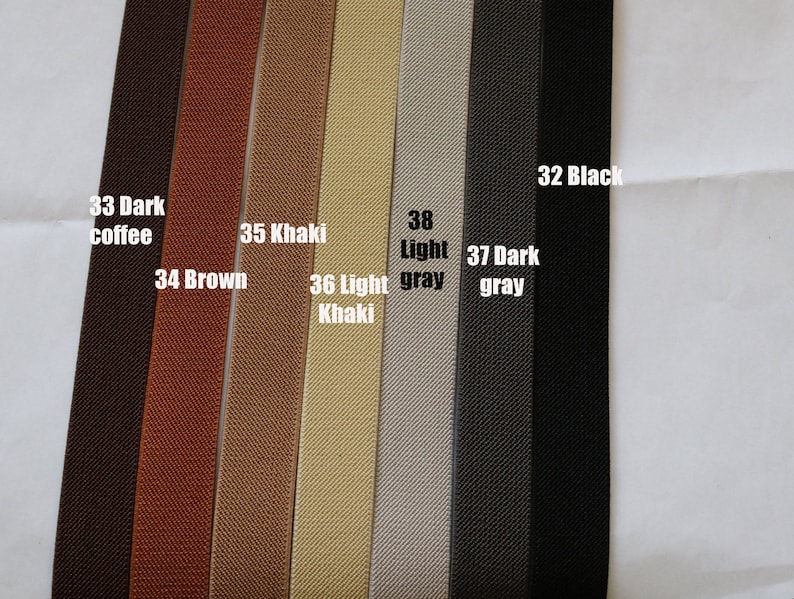 May include: A close-up of eight different coloured elastic bands. The colours are dark coffee, brown, khaki, light khaki, light grey, dark grey, and black. The elastic bands are all the same width and have a textured surface.