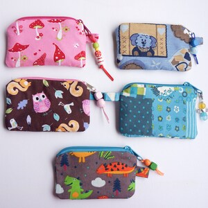 Könnte beinhalten: Fünf kleine Reißverschlusstaschen mit bunten Stoffdesigns und perlenbesetzten Reißverschluss-Zierbändern. Die Taschen sind braun, rosa, blau und grau mit verschiedenen Tier- und Naturmotiven.