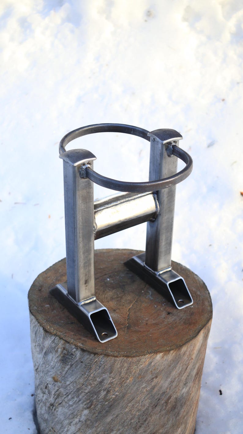 Peut inclure: Support de foyer en m&eacute;tal fait &agrave; la main. Le support est en acier soud&eacute; avec un anneau sup&eacute;rieur circulaire et une base rectangulaire. Il est con&ccedil;u pour maintenir un anneau de foyer et est pr&eacute;sent&eacute; sur une base en bois.