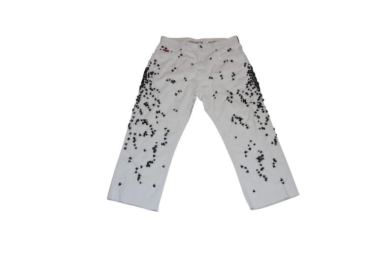 May include: White denim jeans featuring a scattered pattern of small black star-shaped studs concentrated along the outer side seams of both legs, with a standard button fly closure and a visible red brand tag near the waistband.