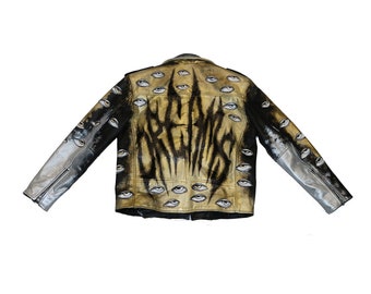 Könnte beinhalten: Eine schwarze Lederjacke mit einem gold-schwarzen Design aus Farbe mit dem Wort "DREAMS" und mehreren gemalten Augen auf der Rückseite. Die Ärmel sind silberfarben.