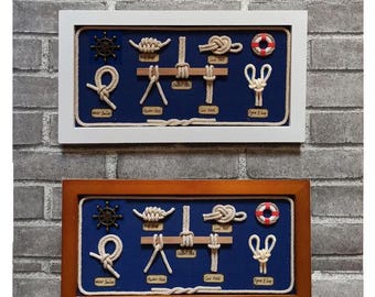 May include: Two framed nautical knot diagrams with a blue background. The top frame is white and the bottom frame is brown. Each frame features a different set of knots, including a figure eight knot, a clove hitch, and a bowline knot. The frames also include a life preserver, a ship's wheel, and the names of each knot.