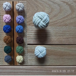 May include: A set of 12 round rope drawer pulls in various colours, including beige, pink, purple, blue, brown, green, grey, and yellow. The pulls are displayed on a wooden board with a woven pattern.