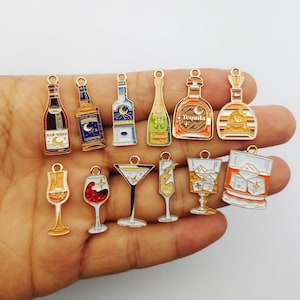 May include: A collection of twelve metal enamel charms shaped like various alcoholic beverage bottles and glasses. The charms feature colourful designs including wine, tequila, vodka, and cocktails with details like stars, moons, and ice cubes.