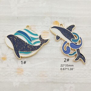 May include: Two gold-tone metal charms featuring a whale design. The first charm is a whale with blue and white waves, the second charm is a whale with blue and white waves and a blue tail fin. The charms are 0.87 inches by 1.38 inches.