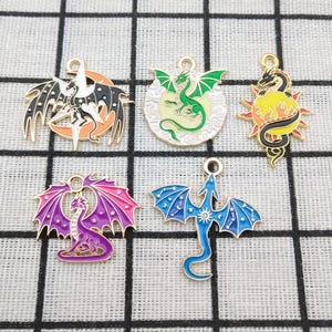 Peut inclure: Collection de cinq breloques dragons colorées. Chaque breloque présente un design de dragon différent avec diverses couleurs, dont le noir, l'orange, le vert, le violet, le bleu et l'or. Les breloques sont en métal et ont une boucle pour les attacher à des bijoux ou à d'autres créations.
