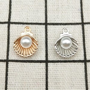 May include: Two gold and silver shell charms with a white pearl inside. The charms have a loop at the top for attaching to jewelry.