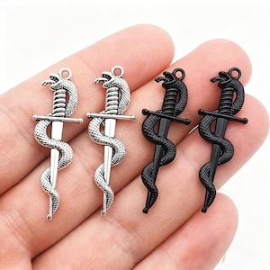 May include: Four metal charms shaped like a dagger entwined with a snake. Two charms are finished in a bright silver tone, and two charms are finished in a matte black tone. Each charm features a small circular loop at the top for attachment.
