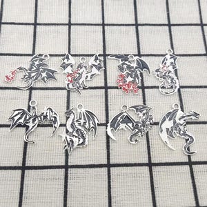 May include: Eight silver-toned metal charms featuring black and white enamel dragon designs. Each charm includes a small loop at the top for attachment. The dragons are depicted in various poses, some with red enamel accents representing fire.
