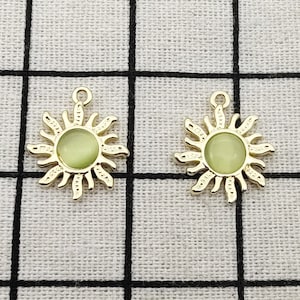 Puede incluir: Dos abalorios de sol de tono dorado con un centro verde que brilla en la oscuridad. Los abalorios tienen un bucle en la parte superior para sujetarlos a joyas u otras manualidades.