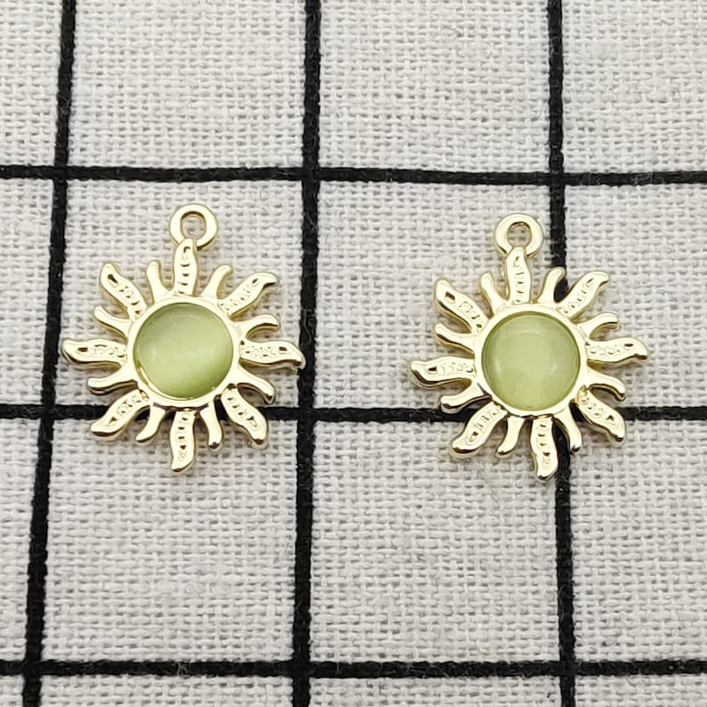 Puede incluir: Dos abalorios de sol de tono dorado con un centro verde que brilla en la oscuridad. Los abalorios tienen un bucle en la parte superior para sujetarlos a joyas u otras manualidades.