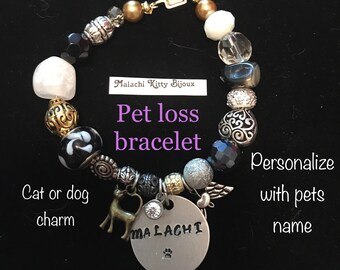 May include: A black and silver beaded bracelet with a silver charm that says "MALACHI" and a small cat charm. The bracelet is for pet loss and can be personalized with a pet's name. The text on the card says "Pet loss bracelet".