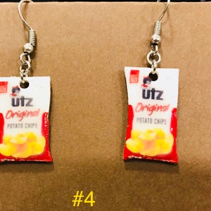 May include: A pair of silver dangle earrings with a miniature Utz Original Potato Chips bag charm. The bag is red, white, and yellow with the Utz logo and text.